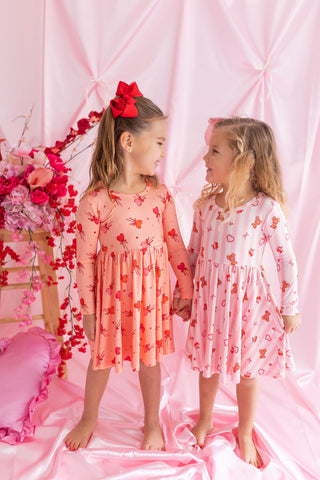 In My Jammers Long Sleeve Twirl Dress - Love You Bear-y Much
Two young girls in pink and red dresses standing against a pink floral backdrop.