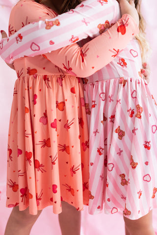 In My Jammers Long Sleeve Twirl Dress - Love You Bear-y Much
Two people wearing matching dresses with heart and bow patterns on a pink background