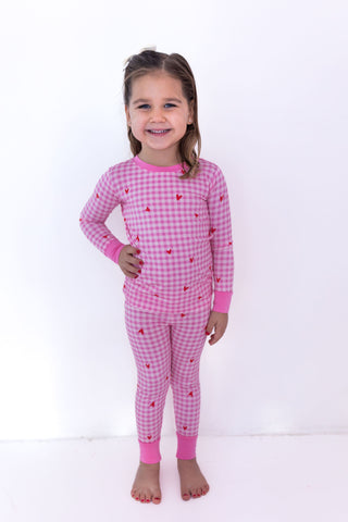In My Jammers Two Piece Set - Be Mine Gingham
Young girl wearing pink checkered pajamas with heart patterns on a white background