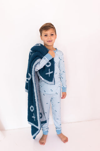 In My Jammers Two Piece Set - Blue XO Gingham
Child wearing a patterned onesie holding a blue blanket with star design on a white background
