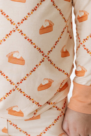 In My Jammers Two Piece Set -  Fall Pie and Leaves 
A close-up of a person wearing a long-sleeve pajama top with a cream background, an orange diamond lattice pattern outlined with small autumn leaves, and pie slice motifs. The cuffs are a solid peach-orange color.