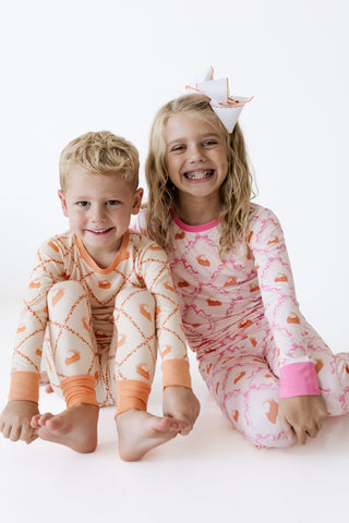In My Jammers Two Piece Set - Fall Pie and Bows
In My Jammers Two Piece Set -  Fall Pie and Leaves
Two children sitting on a white studio floor wearing matching long-sleeve pajamas with a baseball diamond pattern. The boy wears an off-white and orange set, and the girl wears a pink and peach set with a small white bow in her hair.