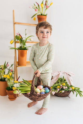 In My Jammers Two Piece Set - Green Little Goose
Child in green pajamas holding an Easter basket with eggs, surrounded by flowers and plants on a white background