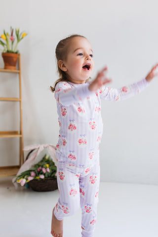 In My Jammers Two Piece Set - Petal Pop
Child wearing a floral onesie in a room with a white wall and wooden shelf.