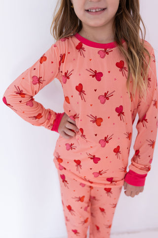 In My Jammers Two Piece Set - Pink Sugar Rush
Child wearing a pink pajama set with heart and bow pattern on a white background