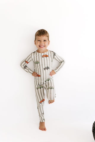 In My Jammers Two Piece Set - Spooky Little Riders
A smiling young boy stands against a plain white background wearing a long-sleeve, full-length striped pajama set with a pattern of small cars and trucks.