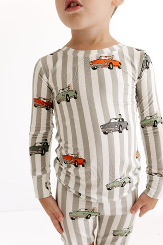 In My Jammers Two Piece Set - Spooky Little Riders
A child wearing a long-sleeve pajama top and matching pants with vertical gray and white stripes and an all-over vintage car print, photographed against a clean white background.