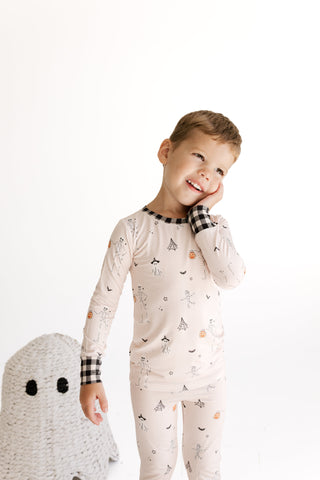 In My Jammers Two Piece Set - The Boo Crew
A young boy wearing a long-sleeve pajama set with a cute ghost and pumpkin print, standing next to a white knit ghost toy against a plain white background.
