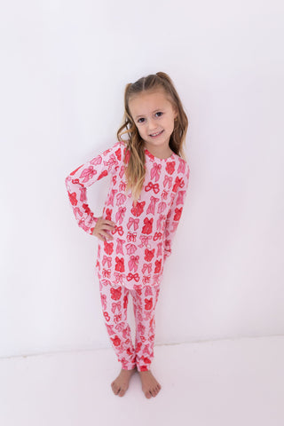 In My Jammers Two Piece Set - Valentine's Bows
Young girl wearing a pink onesie with red patterns on a white background