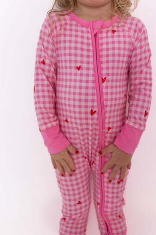 In My Jammers Zipper Romper - Be Mine Gingham
Child wearing pink gingham onesie with red heart patterns on a white background