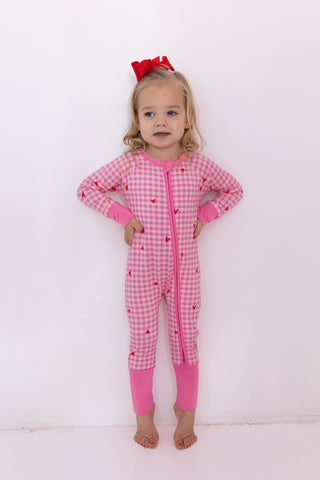 In My Jammers Zipper Romper - Be Mine Gingham
Child wearing a pink checkered onesie with a red bow on a white background