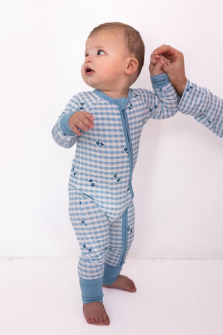 In My Jammers Zipper Romper - Blue XO Gingham
Baby in a blue checkered onesie standing on a white background