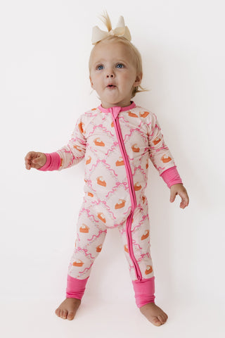 In My Jammers Zipper Romper - Fall Pie and Bows
A baby wearing a pink and white zip-up footed sleeper with an orange and pink pattern, standing against a plain white background.