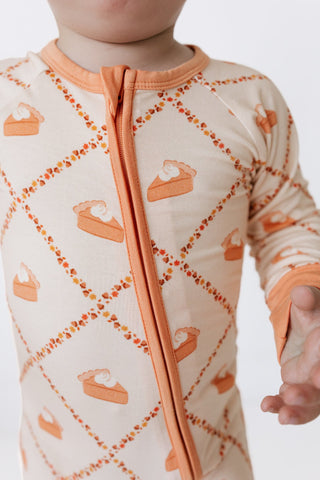 In My Jammers Zipper Romper - Fall Pie and Leaves
A close-up of a baby wearing a long-sleeve cream-colored sleep sack with an orange and brown pie print and a central orange zipper.