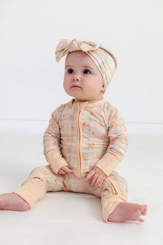 In My Jammers Zipper Romper - Frankie Plaid 
Baby wearing a patterned onesie and headband on a white background