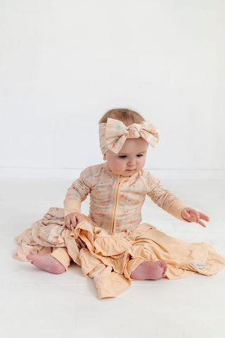 In My Jammers Zipper Romper - Frankie Plaid
Baby in a peach dress with ruffles and a matching headband on a white background