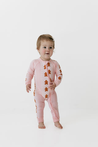 In My Jammers Zipper Romper - Gingerbread Cookies
A baby standing and wearing a pink long-sleeve footless zip-up sleeper with brown gingerbread cookie prints, photographed against a seamless white studio background.