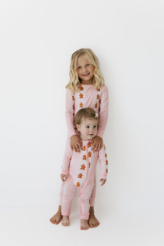 TIn My Jammers Zipper Romper - Gingerbread Cookies
wo young girls modeling matching pink long-sleeve pajamas with orange gingerbread cookie prints, standing against a plain white studio background.