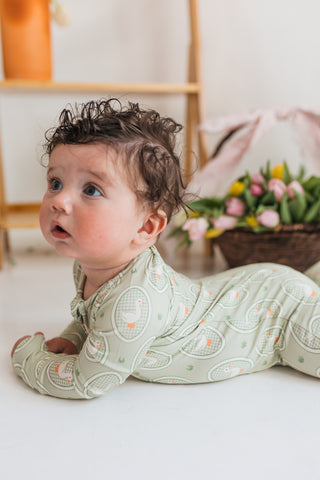 In My Jammers Zipper Romper - Green Little Goose
Baby in a green patterned outfit lying on a white surface with a blurred background
