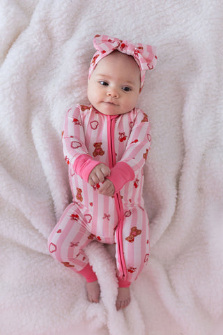 In My Jammers Zipper Romper - Love You Bear-y Much
Baby in pink patterned onesie and headband on a soft white blanket