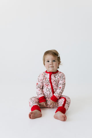 In My Jammers Zipper Romper - Mistletoe Bows
A baby sitting cross-legged on a white studio floor wearing a festive red and white holiday print one-piece pajama with red trim.