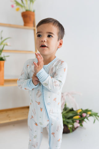 In My Jammers Zipper Romper - Oliver Rabbit
Child wearing a light-colored outfit with a floral pattern in a bright room.