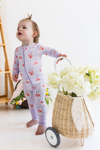 In My Jammers Zipper Romper - Petal Pop
Child in floral pajamas standing next to a basket of flowers on a white floor.