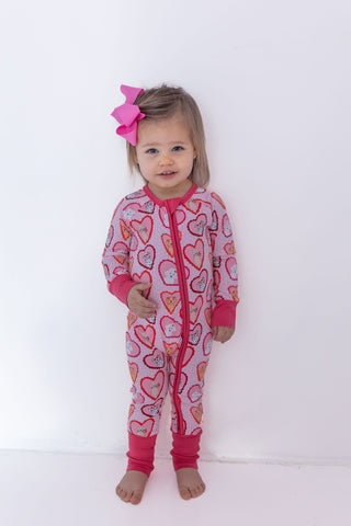 In My Jammers Zipper Romper - Pink Fur-Ever Valentine
Child wearing a heart-patterned onesie with pink accents on a white background