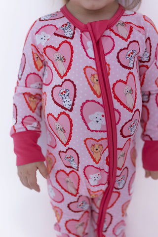 In My Jammers Zipper Romper - Pink Fur-Ever Valentine
Child wearing a pink onesie with heart patterns and cartoon characters on a white background