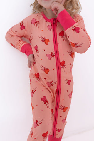 In My Jammers Zipper Romper - Pink Sugar Rush
Child wearing a pink onesie with heart and bow patterns on a white background