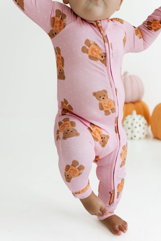 In My Jammers Zipper Romper - Polka Dot Little Boo Bear
A baby wearing a pink footed zip-up sleeper with an orange and brown teddy bear pattern, shown from the waist down against a white studio background with decorative pumpkins.