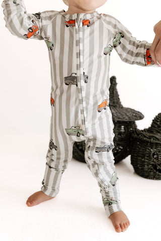 In My Jammers Zipper Romper - Spooky Little Riders
A baby wearing a one-piece zip-up sleeper with vertical gray and white stripes and a print of colorful toy cars, standing barefoot against a white background.