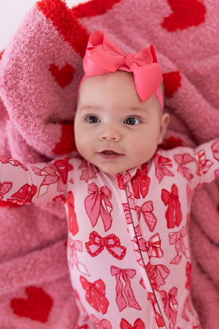 In My Jammers Zipper Romper - Valentine's Bows 
Baby in a pink outfit with red bows and hearts on a pink blanket