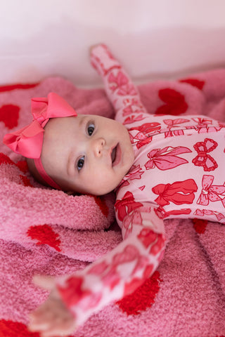 In My Jammers Zipper Romper - Valentine's Bows 
Baby wearing a pink bow and red and white outfit on a pink blanket