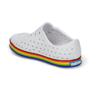 Native Jefferson Wrapped Shoes - Shell White / Rainbow
A white perforated slip-on shoe with a colorful rainbow stripe along the sole and a blue 'native' brand tag on the heel, shown from a side-rear angle on a white background.