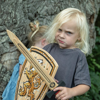 Liontouch Sword - WoodyLion: Gold/Black
Child holding a wooden sword and shield with another child in the background.