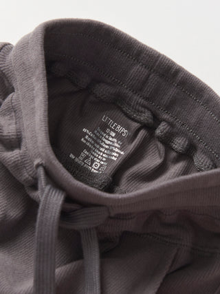 Little Bipsy Ribbed Jogger - Graphite
Close-up of a dark gray hoodie with a brand label on a light gray background