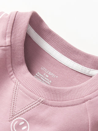 Little Bipsy Smiley Pullover - Dusty Purple
Close-up of a pink sweatshirt with a brand label on the collar.