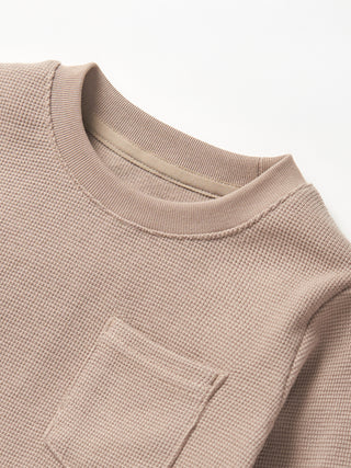 Little Bipsy Waffle Top - Mushroom
Close-up of a textured beige sweater with a pocket on a white background