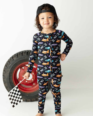 Lev Baby Poppy Convertible Zipper Romper - Elias 
Child wearing a car-themed onesie with a checkered flag and tire in the background