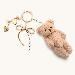 Little Words Project Bag Charm - Doing My Best
A plush teddy bear keychain charm in a light beige bouclé fabric, attached to a gold-tone chain with heart charms, a bow, and a vertical chain reading 'YOU ARE MY BEST'.
