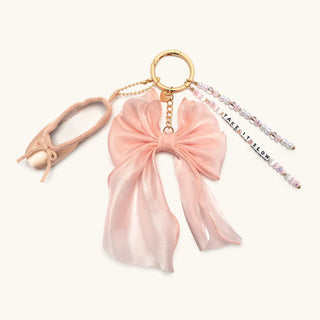 Little Words Project Bag Charm - Take It Slow
A pastel pink ballet-themed keychain featuring a satin bow, a miniature ballet pointe shoe charm, a gold metal key ring, and a beaded chain with the text 'IT'S ALL FLOW'.