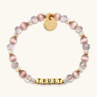 Little Words Project Bracelet - Gold Trust: Grace in Motion
A beaded stretch bracelet featuring dusty pink and lavender faceted beads, gold spacer beads, a round gold charm engraved with 'trust me', and gold letter cubes spelling 'TRUST' on a light cream background.