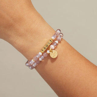 Little Words Project Bracelet - Gold Trust: Grace in Motion
A close-up of a person's wrist wearing a double-strand beaded bracelet in light pink and white beads, featuring a gold bar engraved with 'TRUST' and a small round gold charm.