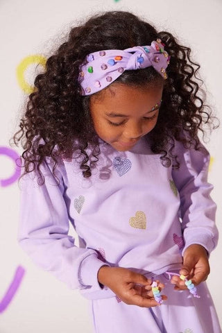 Lola and The Boys Lavender Crystal Hearts Set
Young girl wearing a purple outfit with heart patterns, sitting on a white floor.
