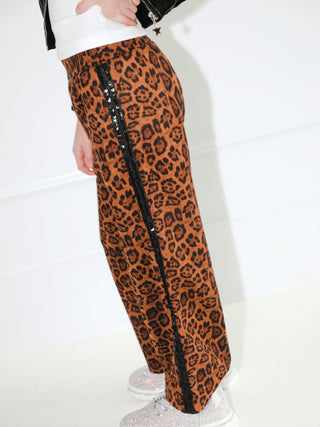 Lola and The Boys Leopard Print Sequin Trim Wide Leg Track Pants
A person wearing leopard-print wide-leg pants with a black sequined side stripe, paired with a white top and sparkly silver shoes, photographed indoors against a white wall.