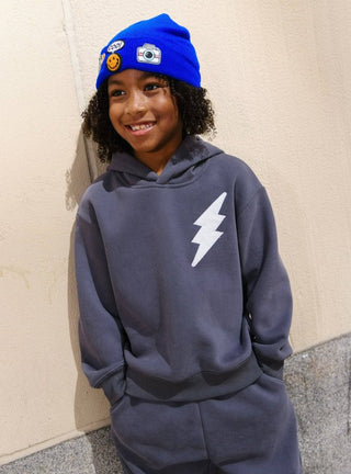 Lola and The Boys Lighting Flash Set - Grey
Person wearing a blue hoodie with a lightning bolt design and a blue beanie with stickers.