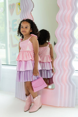 Lola and The Boys Pastel Ombre Shimmer Bow Dress
Young girl in a pink and purple dress standing in front of a mirror with wavy pink and white frame.