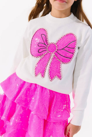Lola and The Boys Pinky Big Bow Sweater
Child wearing a white sweater with a pink bow design and a pink skirt.