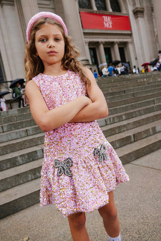 Lola and The Boys Rosie Bows Dress Young girl in a pink floral dress with butterfly accents standing on steps in an urban setting.
